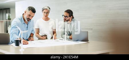 Team of creative businesspeople making drawings on wind turbine blueprints. Innovative design professionals brainstorming while working on a renewable Stock Photo