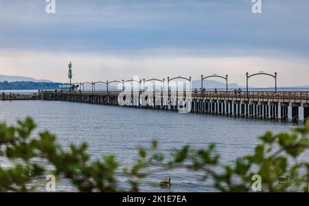 Wooden pier at White Rock, BC, Canada extends diagonally into image. City of White Rock Pier at overcast cloudy day, British Columbia, Canada. Travel Stock Photo