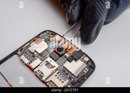 a smartphone repairman takes out a photo module from a smartphone with tweezers. Stock Photo