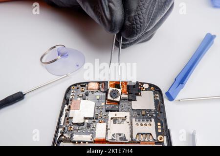 a smartphone repairman takes out a photo module from a smartphone with tweezers. Stock Photo