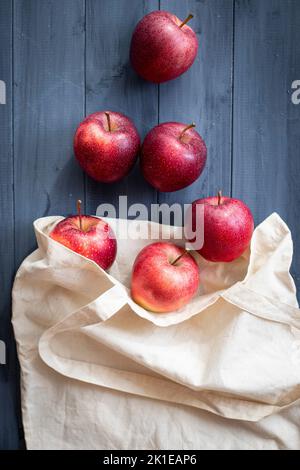 Red apples in white fabric reusable bag placed on wooden table. Eco-friendly packaging concept. Top view. Stock Photo