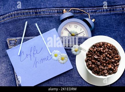 blue alarm clock with coffee beans espresso coffee cup over jeans or denims pocket like concept time and love for coffee or morning coffee or coffee t Stock Photo
