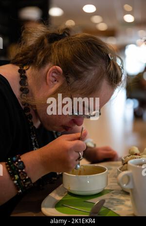 Lifestyle portrait of a 39 year old white woman with Down Syndrome eating in a restaurant, Tienen, Belgium Stock Photo