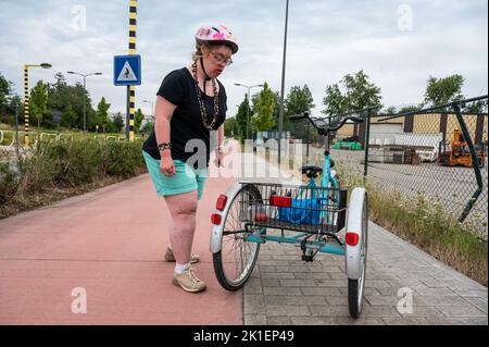 Tienen, Flemish Brabant, Belgium - 08 20 2022 - 39 yo white woman with Down Syndrome standing next to her tricycle on a biking trail Stock Photo