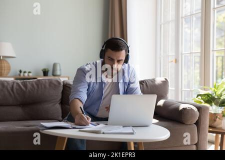 Concentrated millennial adult student man in wireless headphones studying online Stock Photo