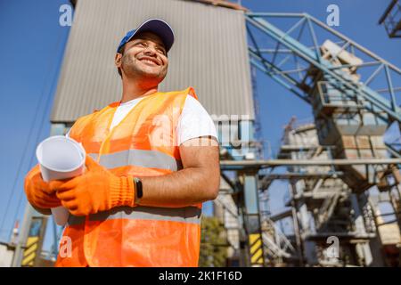 Happy construction engineer working on blueprint at plant Stock Photo