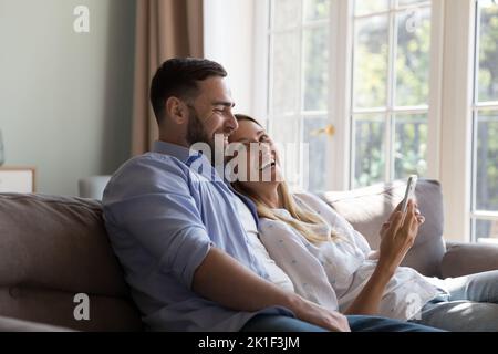 Happy cheerful married couple relaxing, hugging on couch at home Stock Photo