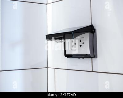 Close-up empty white electrical plug socket plate panel with transparent plastic shield on tiles in bathroom wall. Socket with protection shell waterp Stock Photo