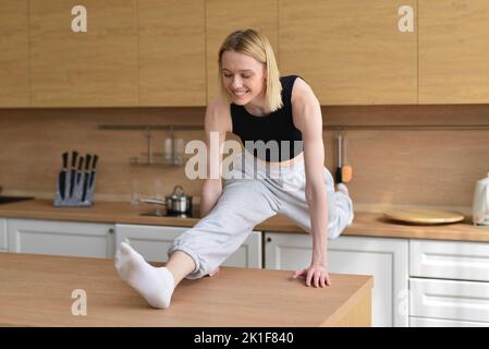 Woman doing the splits in kitchen between tables. Stock Photo