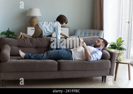 Relaxed dad resting on sofa, holding mobile phone Stock Photo