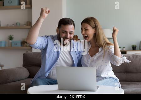 Cheerful excited millennial husband and wife making winner yes hands Stock Photo