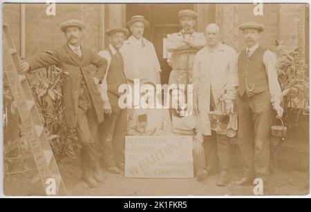 Photograph of painters and decorators in the early 20th century. The men are standing behind a sign advertising the firm of W. Barton junior, 2 Kimberley Road, Croydon, and are holding paint brushes, pots / buckets, a sweeping brush and other pieces of equipment. They are wearing a mix of working clothes (e.g. overalls) and smarter suits for the photographer. The man on the left of the image is posing with one hand on his hip whilst leaning on a ladder with 'Barton decorator' stamped on the side. Stock Photo