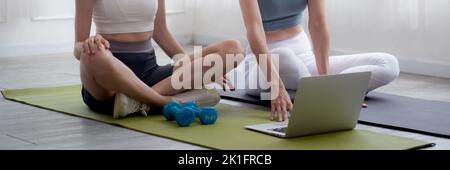 Young woman practicing exercise or yoga on mat while watching laptop computer tutorial online at home, woman having motivation looking notebook for wo Stock Photo