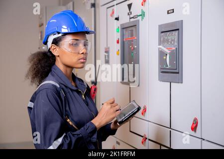 Electrical young asian woman engineer examining maintenance cabinet system electric and using tablet in control room at industrial factory, technician Stock Photo