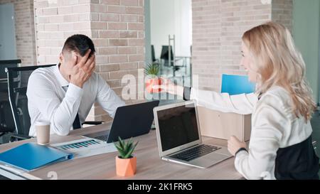 CO-workers in an office, one of them happily giving a gift and the second looks shy Stock Photo