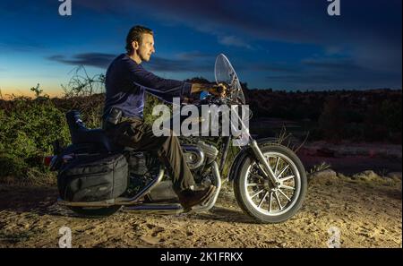 A man sitting on a Harley Davidson Motorcycle ready for a road trip in Arizona in Prescott Valley at night Stock Photo