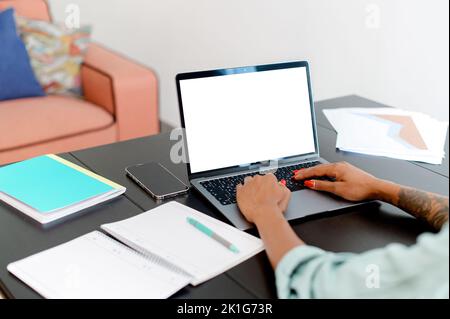Photo over the shoulder of the woman sitting in front of laptop and looking at blanc empty laptop screen, viewing, texting, using new modern fast communication app, mockup, copy space Stock Photo