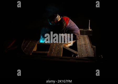 Worker with protective mask welds huge metal carcass in shop Stock Photo