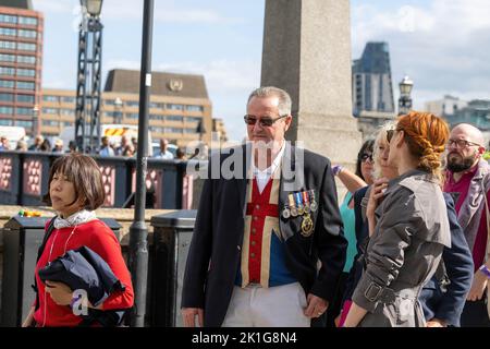 Man with medals and union flag waistcoat waits in a queue on Lamberth Bridge to view The Queen's coffin. Large crowds of mourners visit Westminster Hall to view the Queen's coffin.