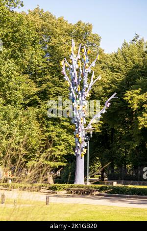 A gray tree full of colored bird cages stacked on top of each other with a green tree background Stock Photo