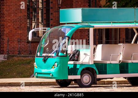 A green tourist bus with white seats located in the middle of the city center in front of a brown old brick building Stock Photo