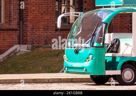 A green tourist bus with white seats located in the middle of the city center in front of a brown old brick building Stock Photo