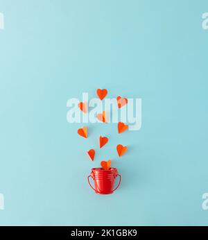 Red paper hearts flying out of the red metal bucket on a blue background. Minimal concept. Stock Photo