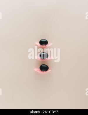 Easter flat lay background with three black eggs on pink feathers against pale pink surface. Minimal concept. Stock Photo