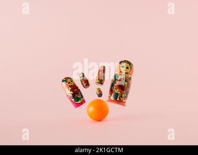Russian dolls known as matryoshka or babushka as the pins flying from the strike of the orange bowling ball on a pink background. Minimal concept. Stock Photo
