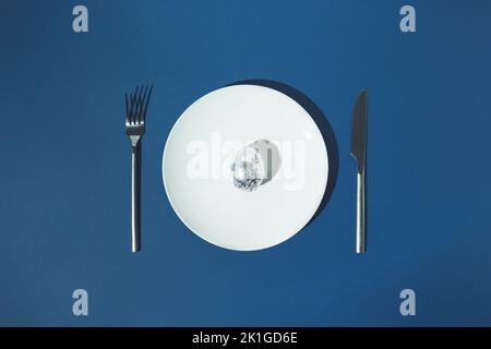 Egg in aluminium foil on white plate with fork and knife on a side on blue background. Stock Photo
