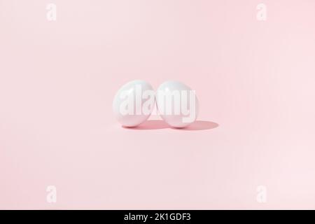 Easter scene with two white eggs leaning against each other on pink background. Stock Photo