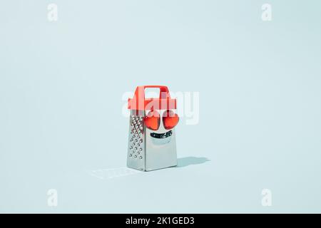 Metal grater with heart-shaped glass eyes on blue background. Minimal food concept idea. Stock Photo