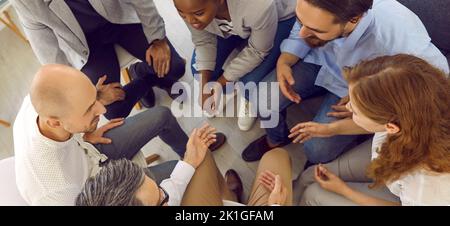 Cheerful and friendly team of office colleagues sitting in circle and chatting during work break. Stock Photo