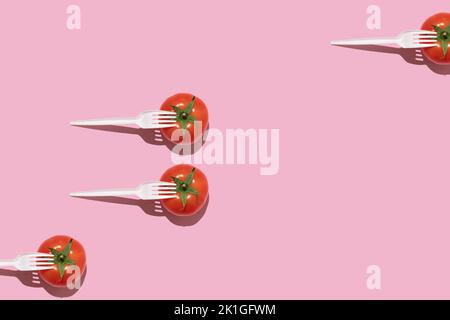 Creative food concept. Fresh tomatoes with white plastic forks on a pink background. Stock Photo