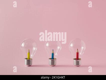 Yellow, blue and red wooden crayons inside the light bulbs on pale pink background. Minimal concept. Stock Photo