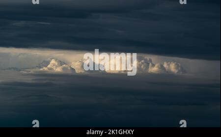 Bright sunlit cloud visible through opening in dark cloud, abstract landscape Stock Photo