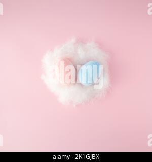 Easter scene with pink and blue eggs in white feathered nest on pink background. Stock Photo
