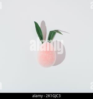 Pink plush egg with fresh leaves as bunny ears on white background. Stock Photo