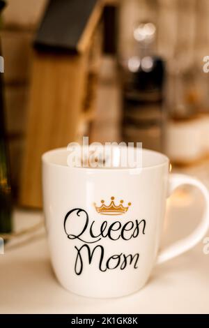 A white cup with the inscription Queen Mama stands on the table in the kitchen Stock Photo