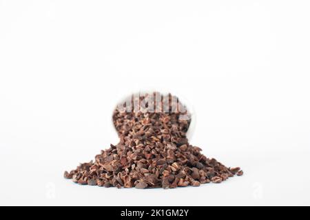 Heap of organic raw cacao nibs, with full of white ceramic bowl on back. Super food isolated on white background. Stock Photo