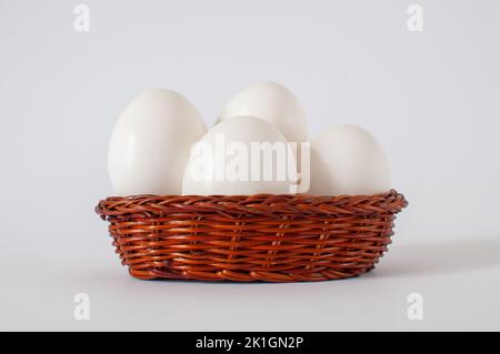 Group of fresh, raw white chicken eggs in mini brown wicker basket isolated on white background with selective focus. Stock Photo