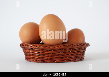 Profile view of fresh, natural brown chicken eggs in mini wicker basket. Isolated on white background with selective focus. Stock Photo