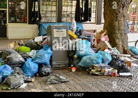 Amsterdam, Netherlands - August 2022: Piles of rubbish bags dumped alongside a waste bin on a street in the centre of Amsterdam Stock Photo
