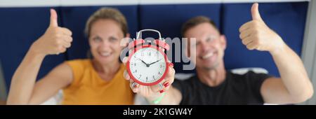 Married couple is holding alarm clock and thumbs up gesture Stock Photo