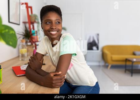 Portrait of dreamy african young woman sitting at desk in modern home studio Stock Photo