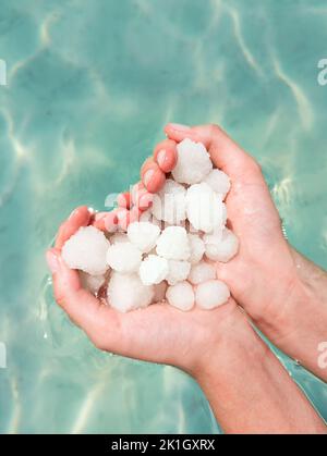 Hands holding sea salt crystals heart-saped on sea water background Stock Photo