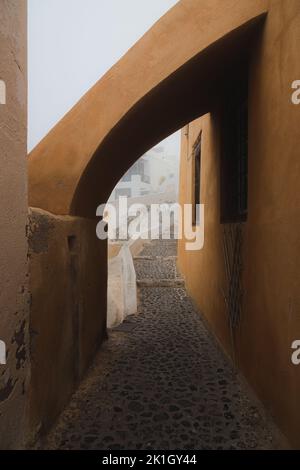 Quiet, narrow, cobblestone street path on a foggy, misty morning in the old town village of Oia, on the Greek Island of Santorini, Greece.