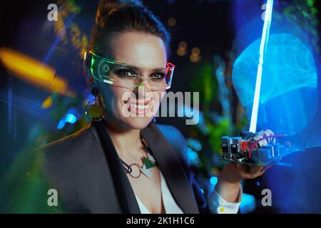 Portrait of happy trendy female with futuristic goggles and electronic board in metaverse. Stock Photo
