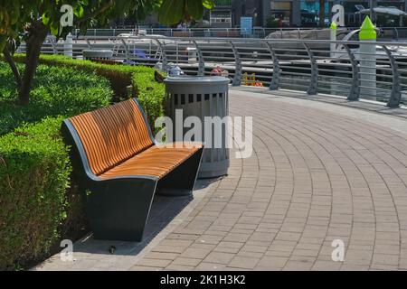 Empty contemporary wooden bench along trimmed green plant fence and curved pavement. Urban modern public furniture. Stock Photo