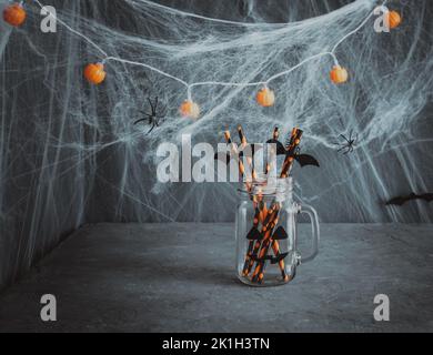 Halloween decorations. A glass jar with drinking straws on dark background with cobwebs. Copy space. Stock Photo